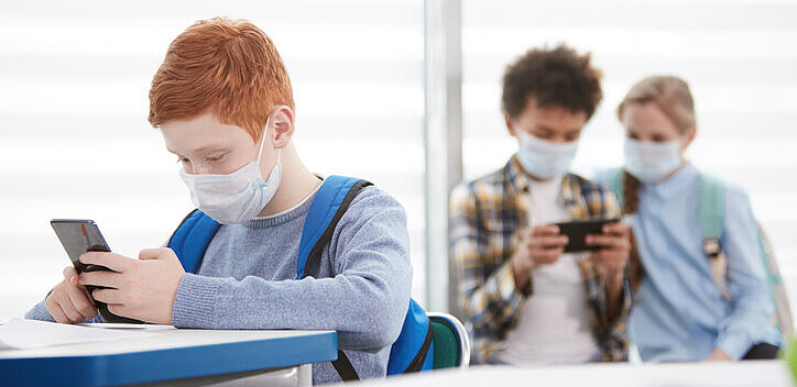 istock.com/SeventyFour Abbildung zeigt einen Schüler alleine und zwei andere Schüler, die sich jeweils mit ihrem Handy beschäftigen