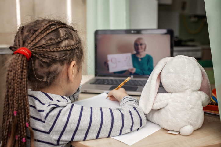 Abbildung zeigt Schülerin, die zuhause vor einem Laptop sitzt, und an einer Online-Unterrichtsstunde teilnimmt.