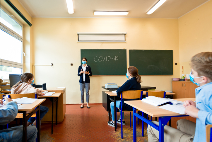 Abbildung zeigt eine Unterrichtsstunde, bei der alle Personen eine Maske tragen